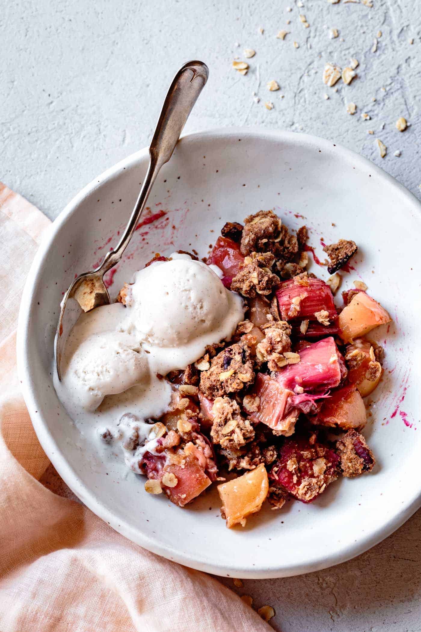 apple rhubarb dessert with crisp topping and ice cream in a white bowl