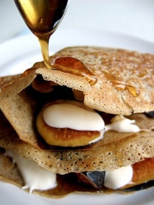 syrup being poured onto stack of buckwheat crepes