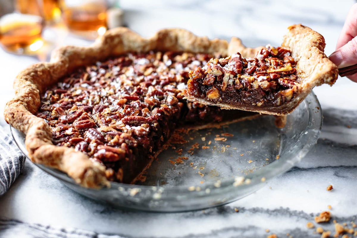 a slice of maple bourbon pecan pie is being removed from the pie plate