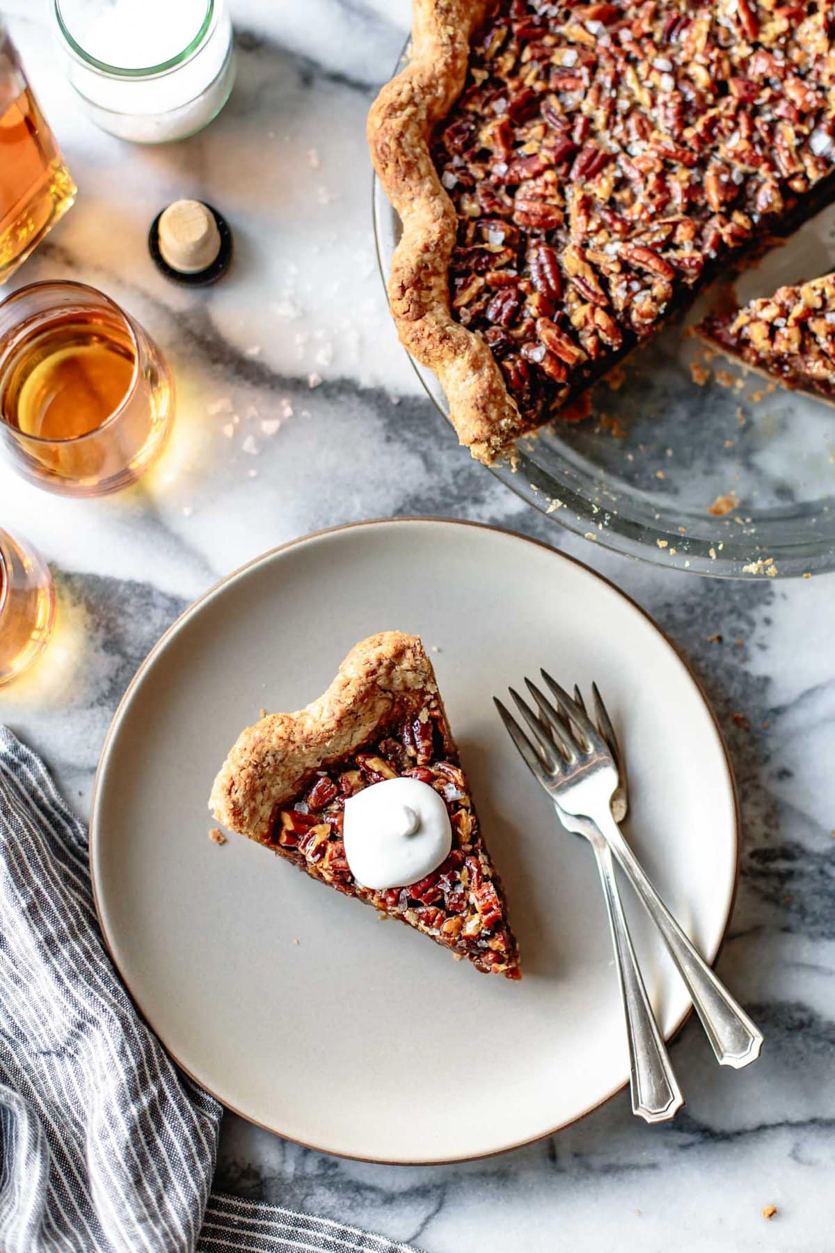 a piece of gluten-free pecan pie is on. a beige plate topped with whipped cream and two forks