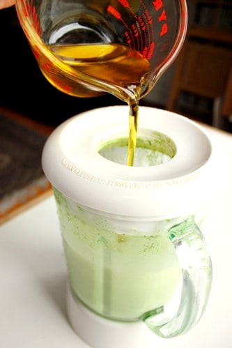 olive oil being poured into a blender 