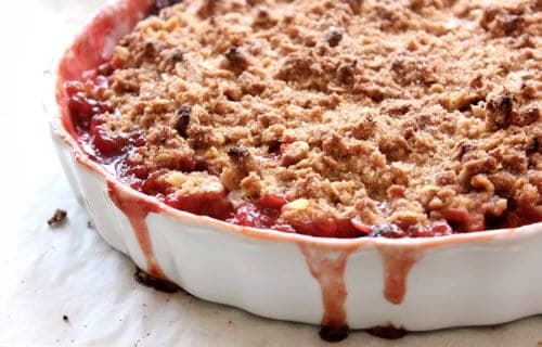 gooey gluten-free strawberry rhubarb crisp is shown fresh out of the oven with juice dripping down the sides of the white pan