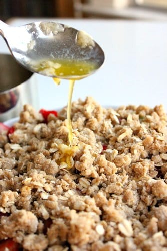 butter is being drizzled over the uncooked crumble topping 