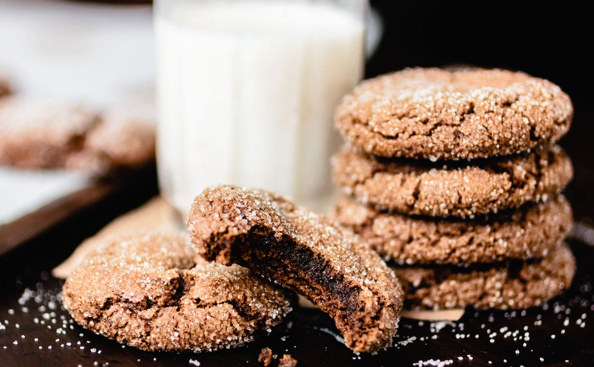 Ginger molasses cookies have been stacked haphazardly. One cookie has been bitten into revealing a moist and gooey middle.