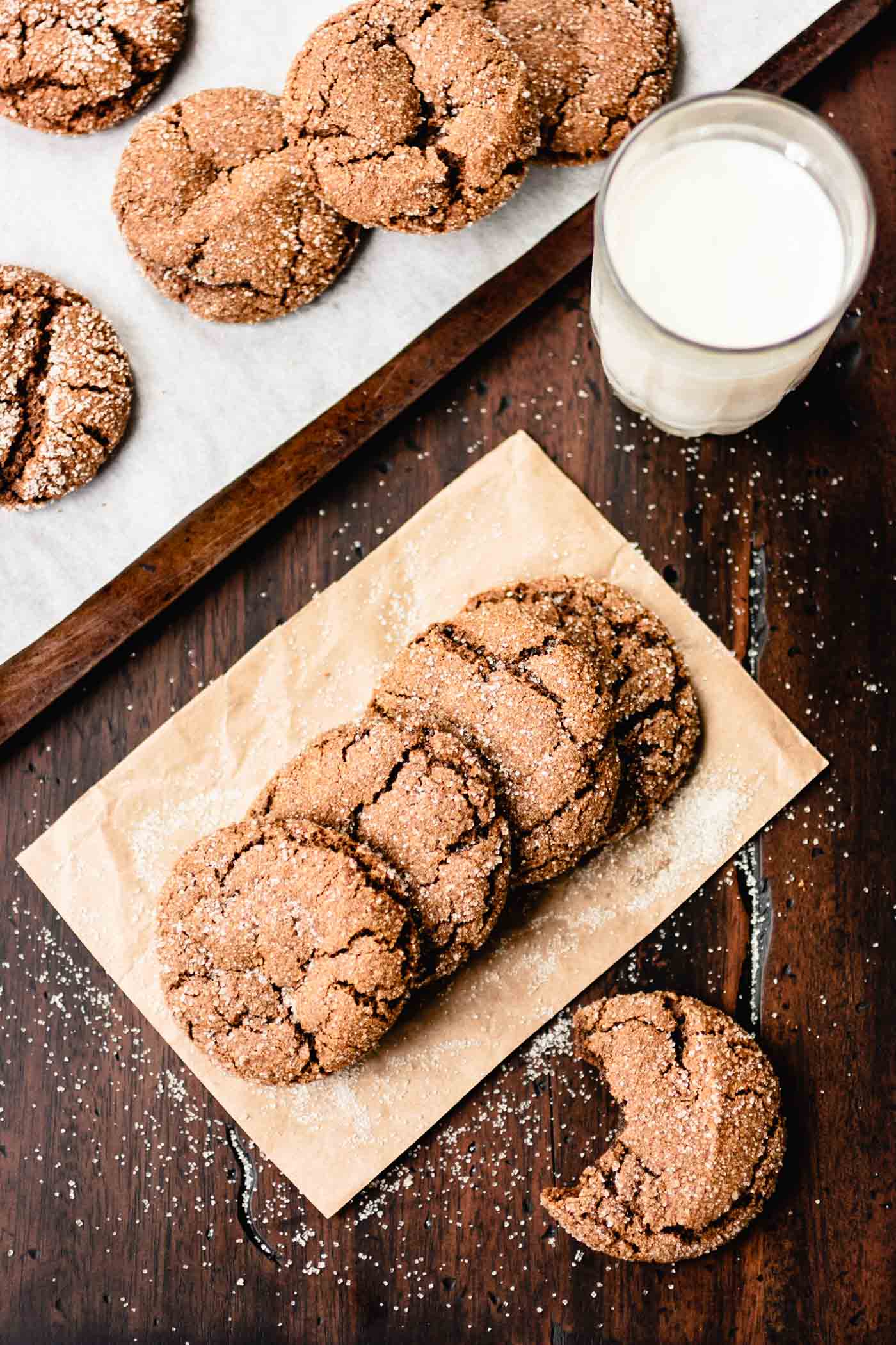 A row of sugar-topped cookies sits on a square of parchment paper with a glass of milk alongside it