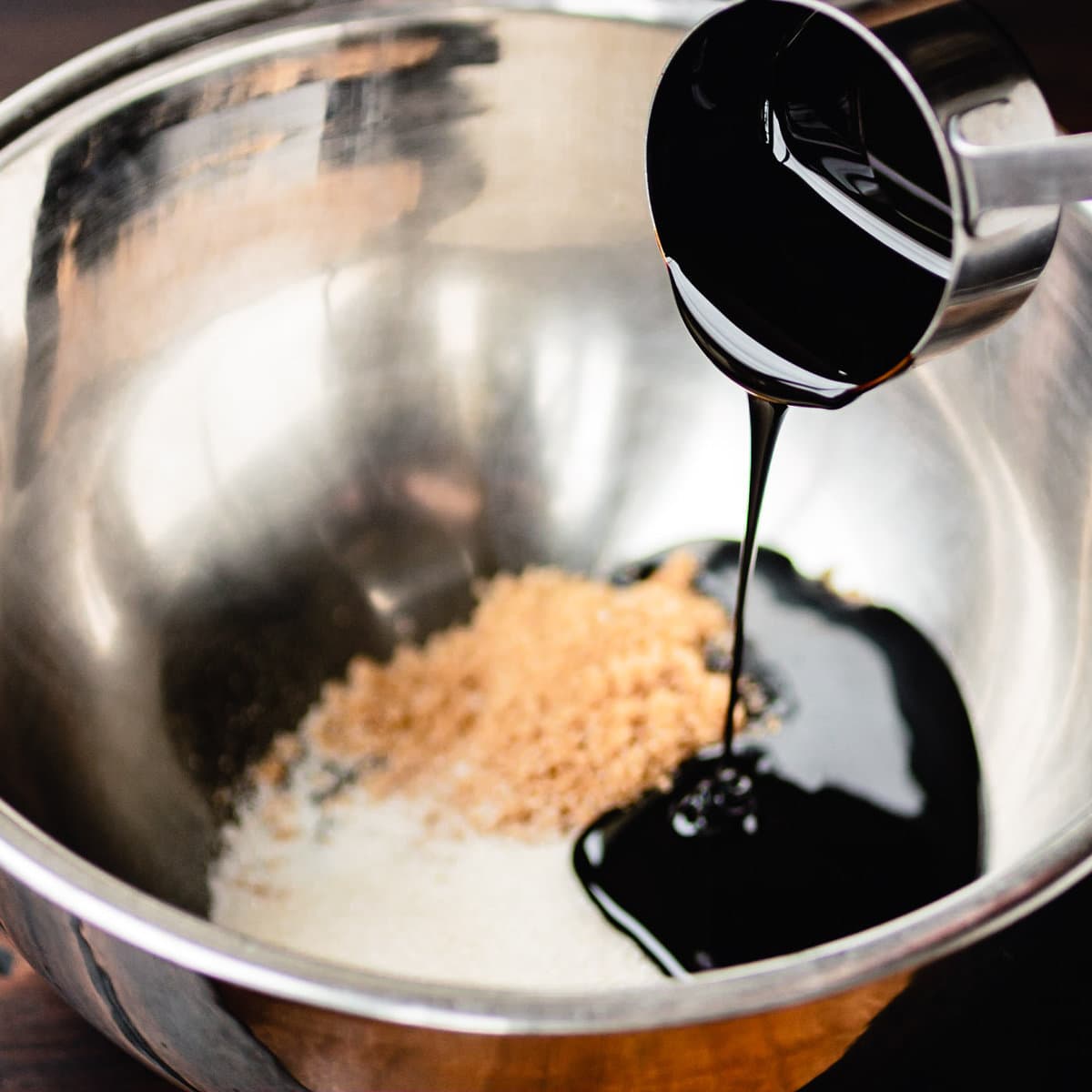 Molasses is being poured into a large mixing bowl with white and brown sugar