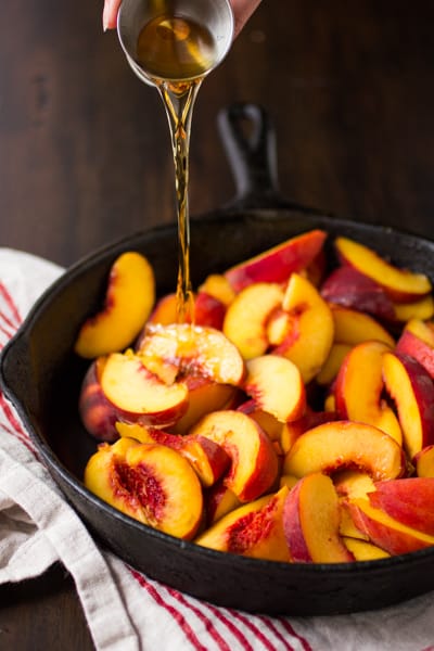side shot of bourbon bing poured into skillet of peaches 