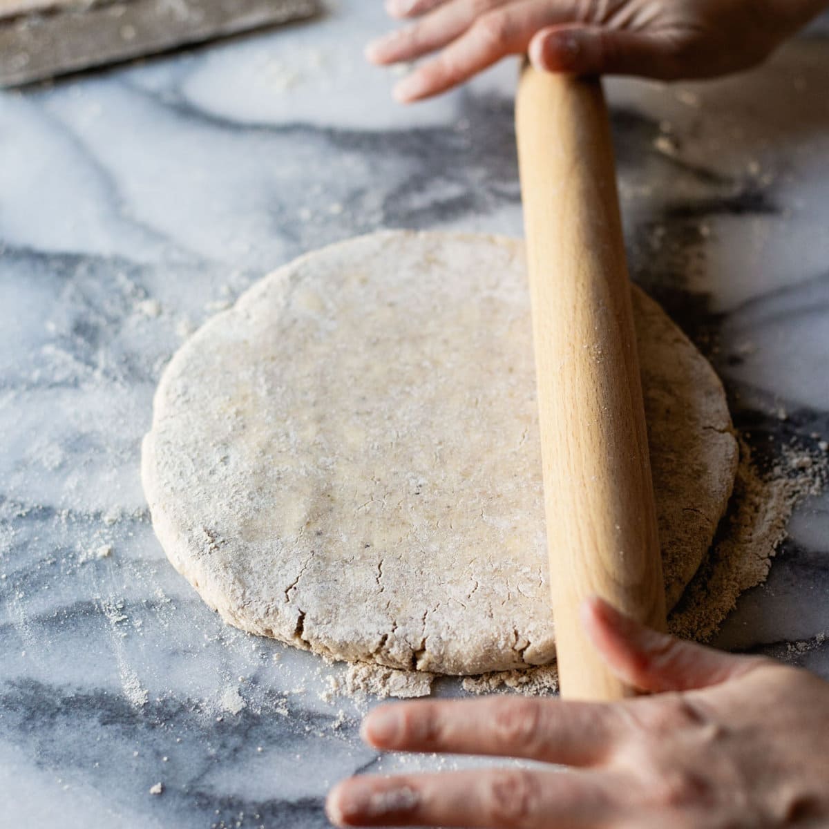 hands are rolling out the gf pie dough with a wood rolling pin