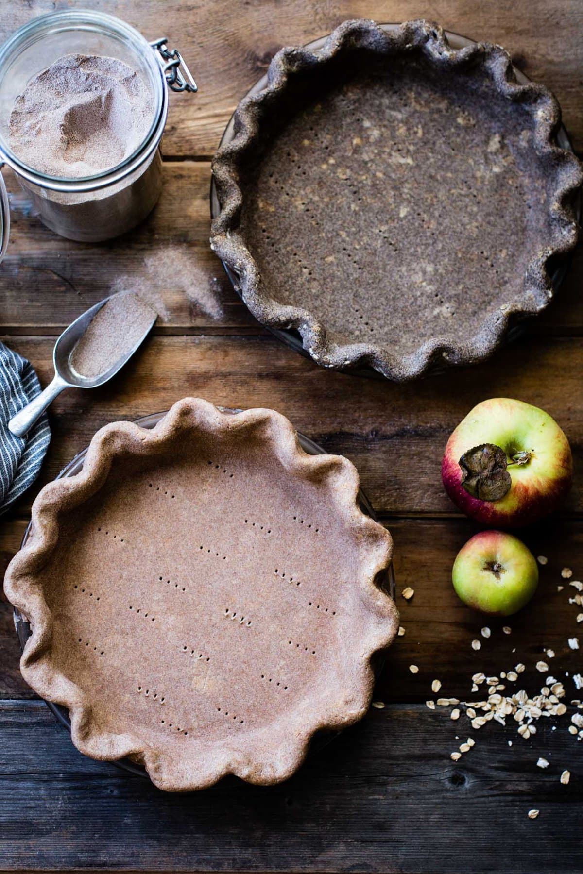 Two unbaked pie crusts sit on a wood surface, one tan colored from teff flour, the other deep gray-brown from buckwheat flour