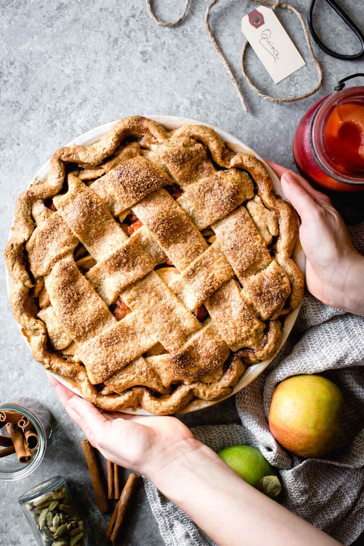 Hands are placing a handsome lattice-topped pie on a gray surface