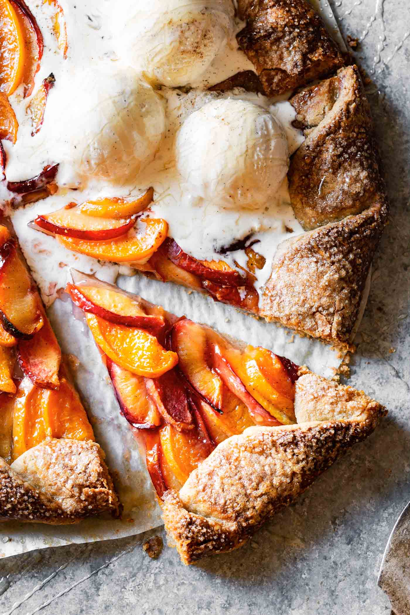 A colorful galette with crispy crust and glossy orange and red fruit has been sliced and topped with melty ice cream