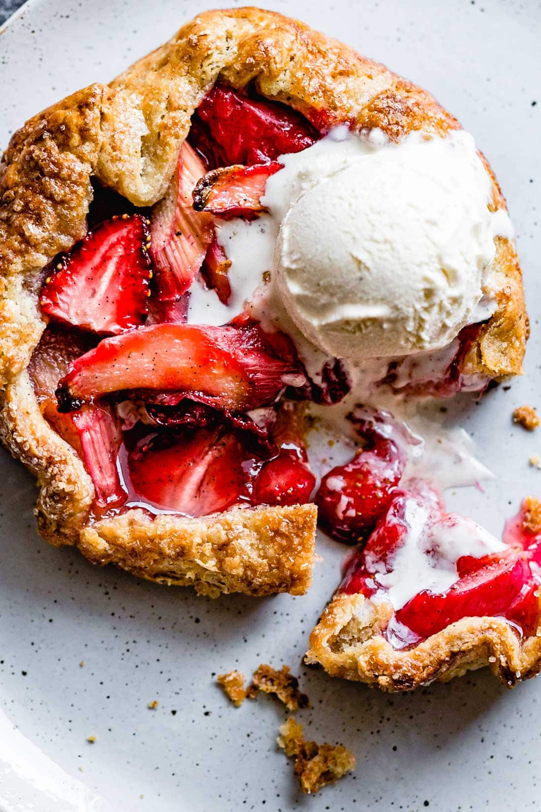 A very sexy close-up of a berry rhubarb galette showing flaky AF crust, gooey fruit, and a scoop of melty ice cream