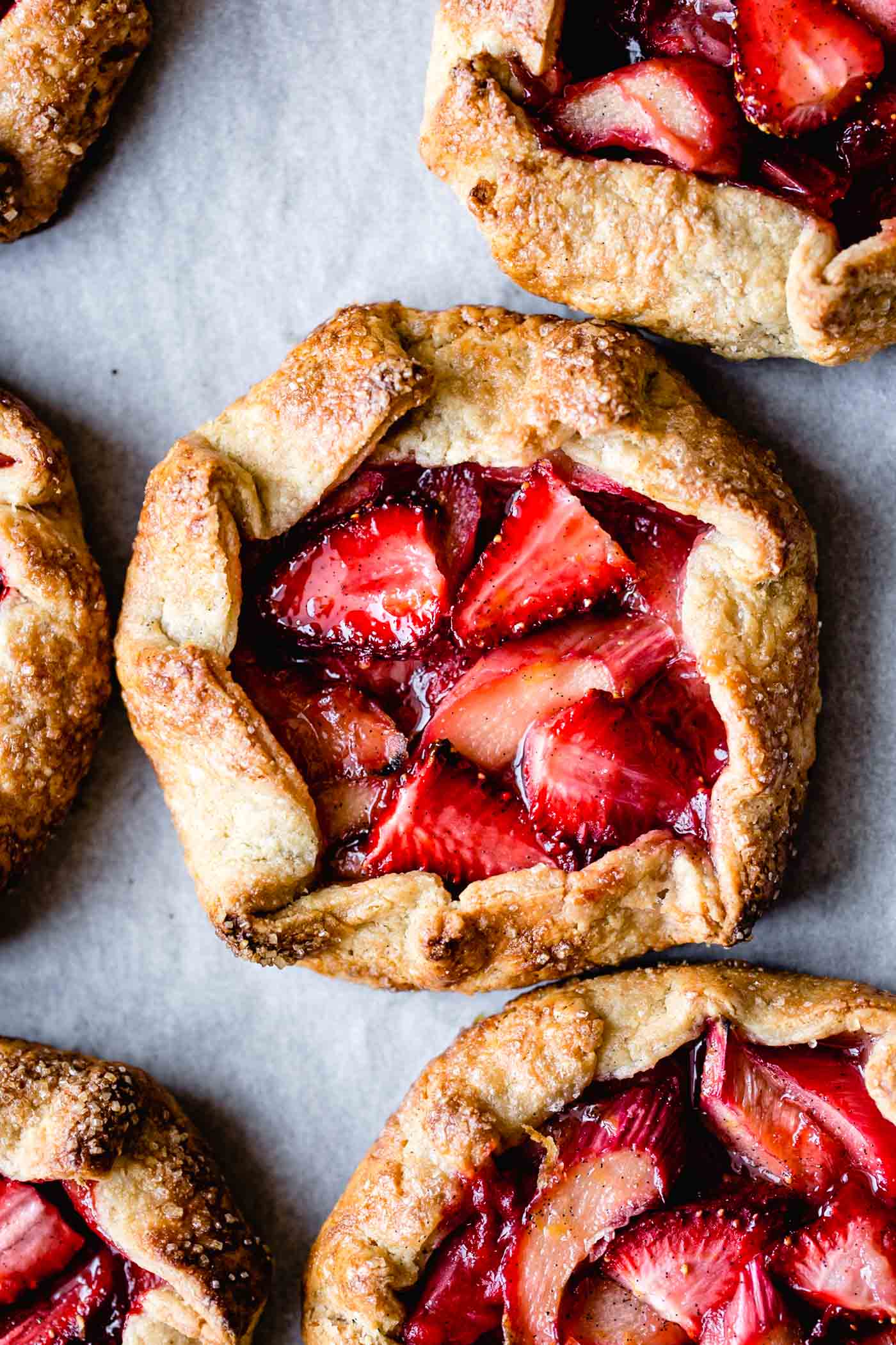 Cute mini galettes stuffed with berries and rhubarb are on a baking sheet