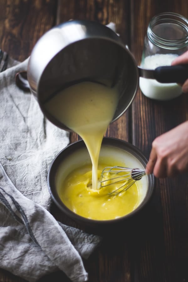 pouring hot cream into egg yolks while whisking
