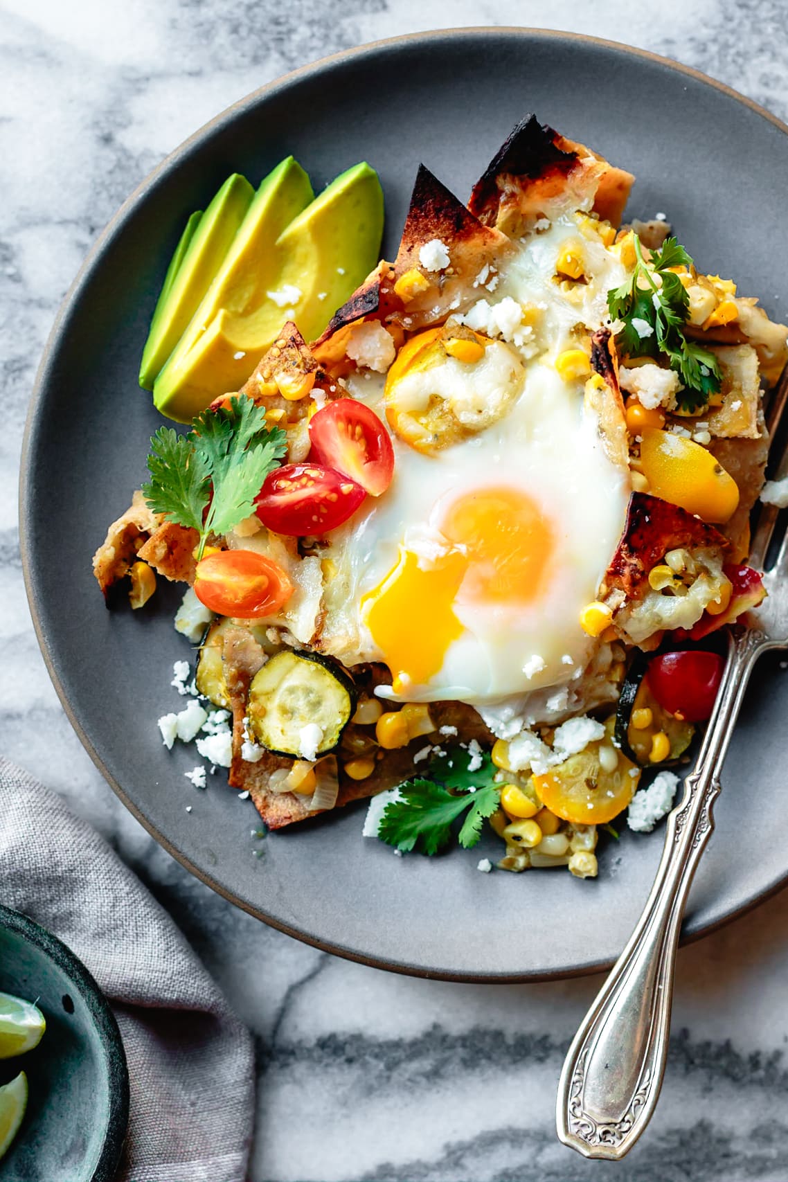 green chilaquiles with loads of veggies, avocado, and a runny baked egg