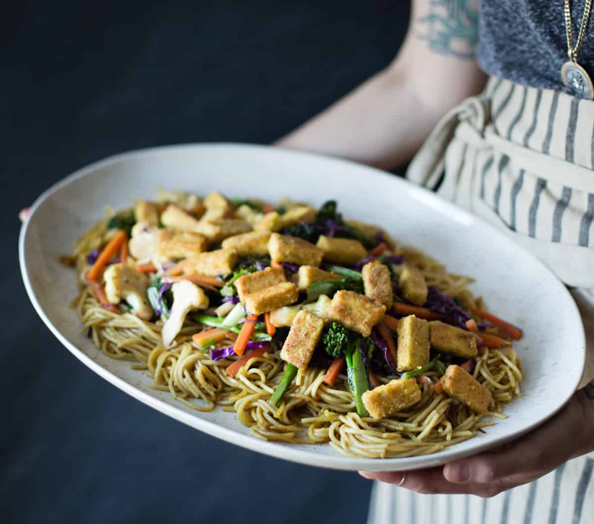 chef holding big dish of Curried Noodles with Crispy Tofu & Winter Vegetables {gluten-free & vegan}