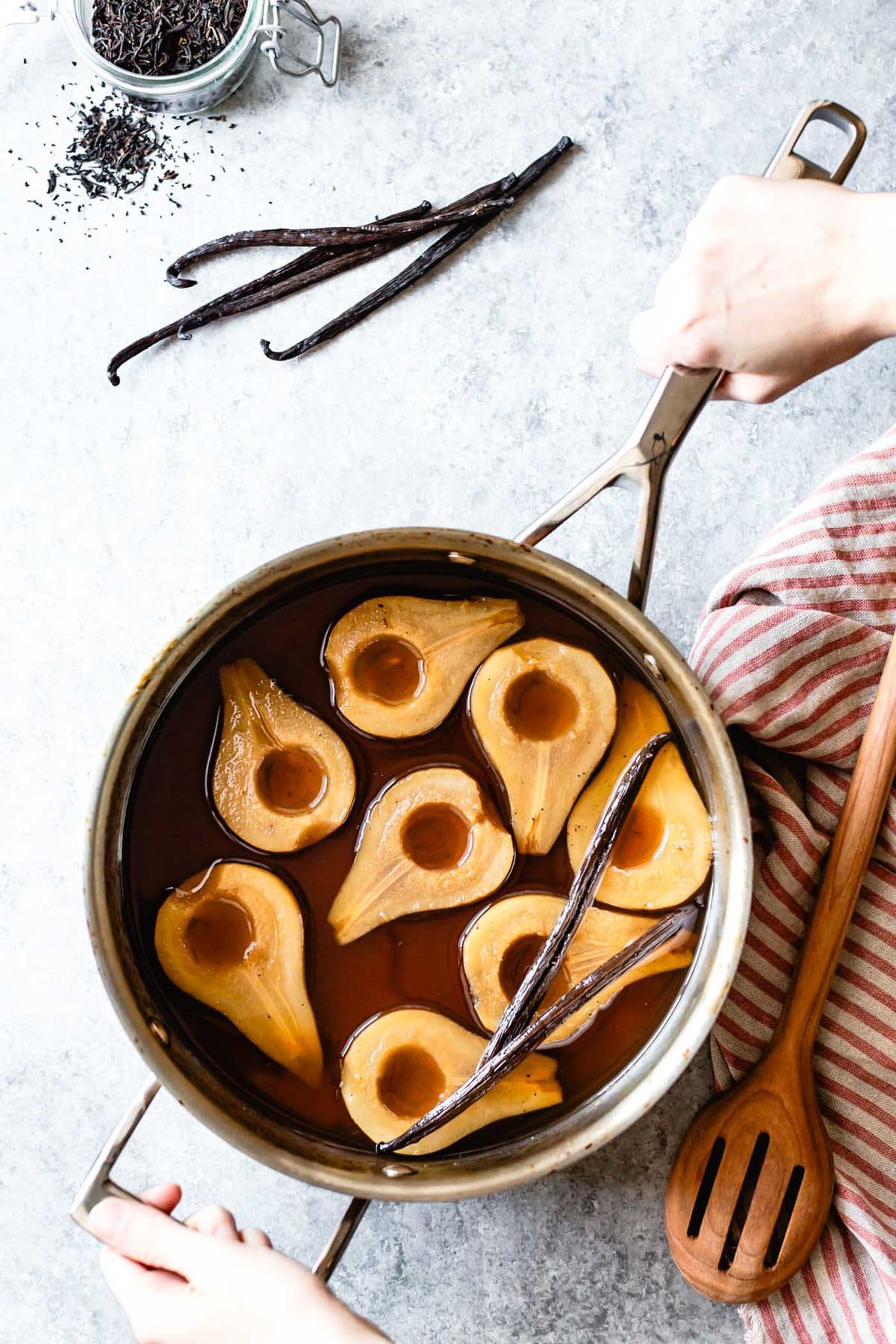 Hands are holding a pot of poached pears in tea