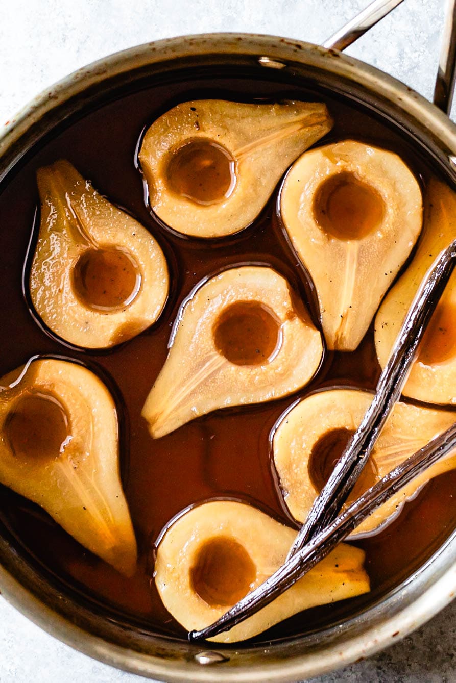 beautiful tea poached pears are in a saucepan flecked with vanilla bean seeds