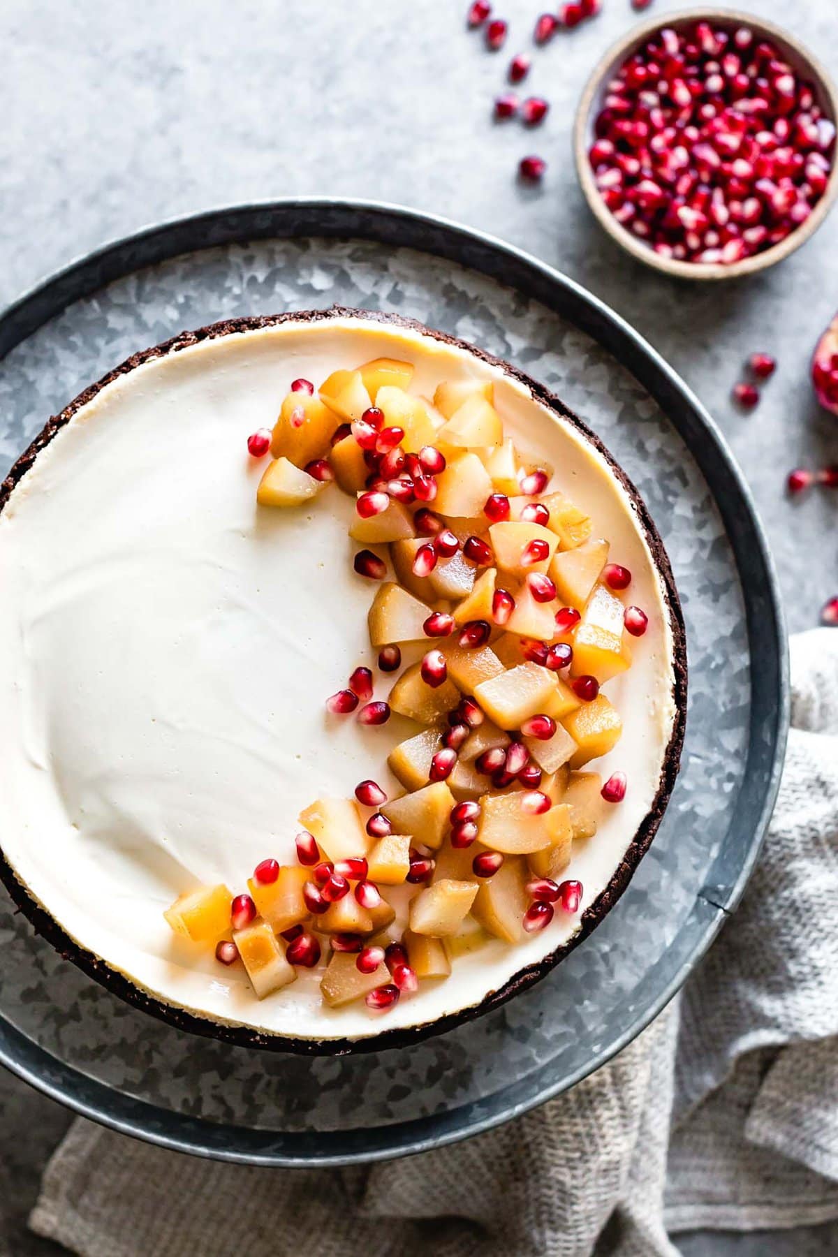 the baked cheesecake has been topped with poached pear chunks and pomegranate arils in a half moon pattern