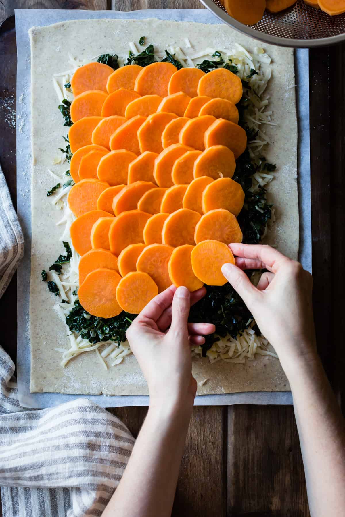 hands are arranging sweet potato slices over the kale