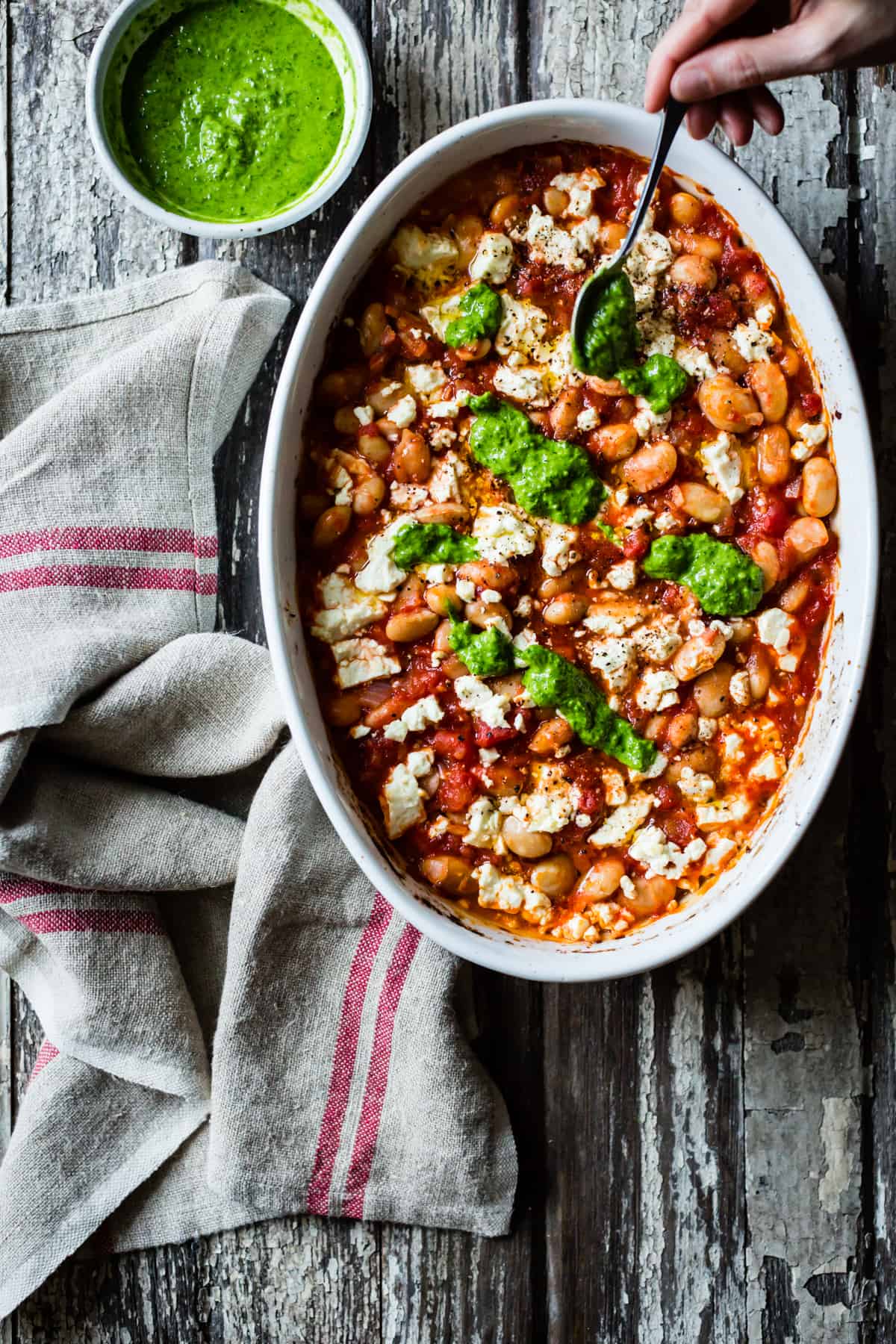 spooning sauce on Tomato Baked White Beans with Feta and Lemon Parsley Oil