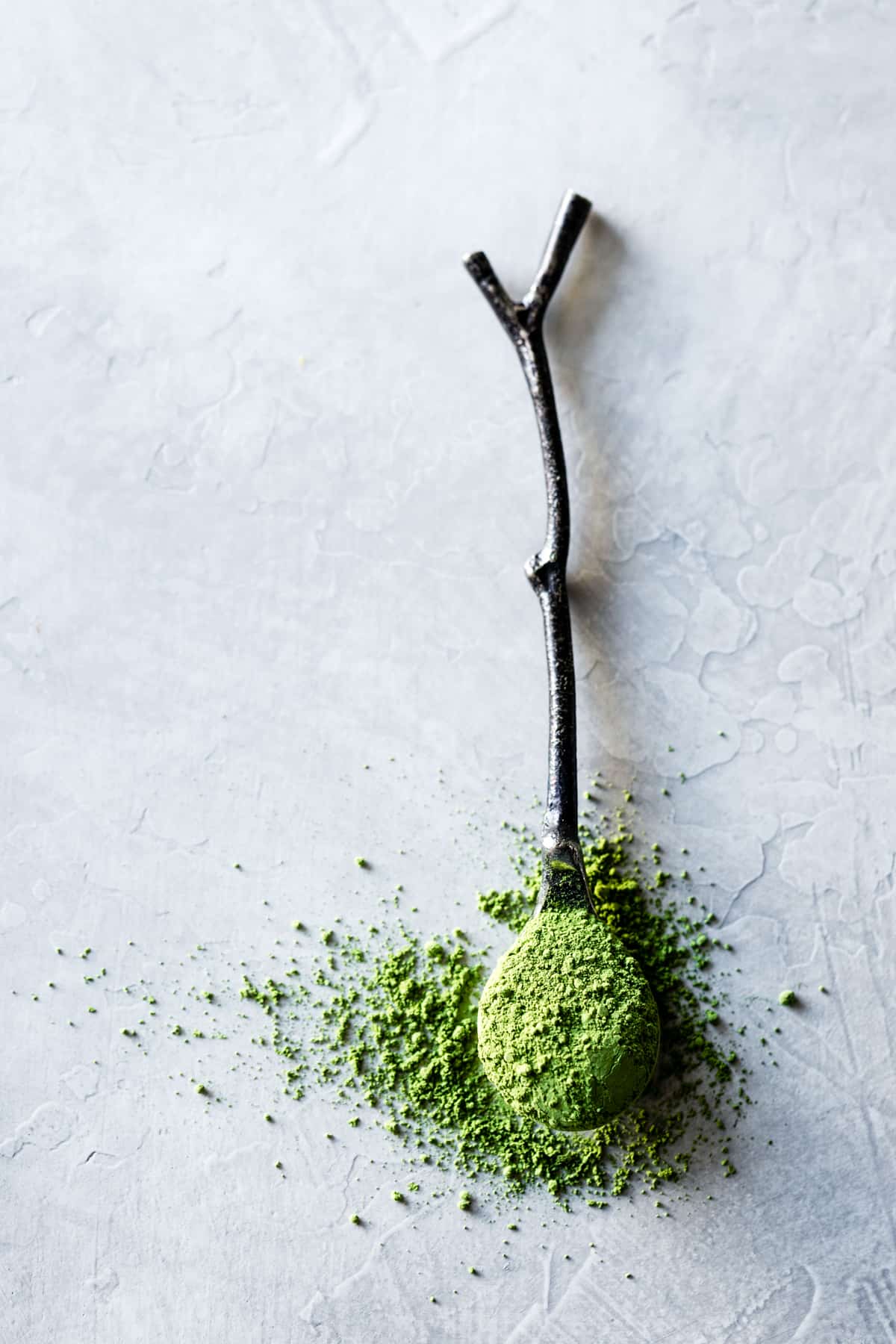 matcha green tea powder on a spoon that looks like a twig, on a plaster surface