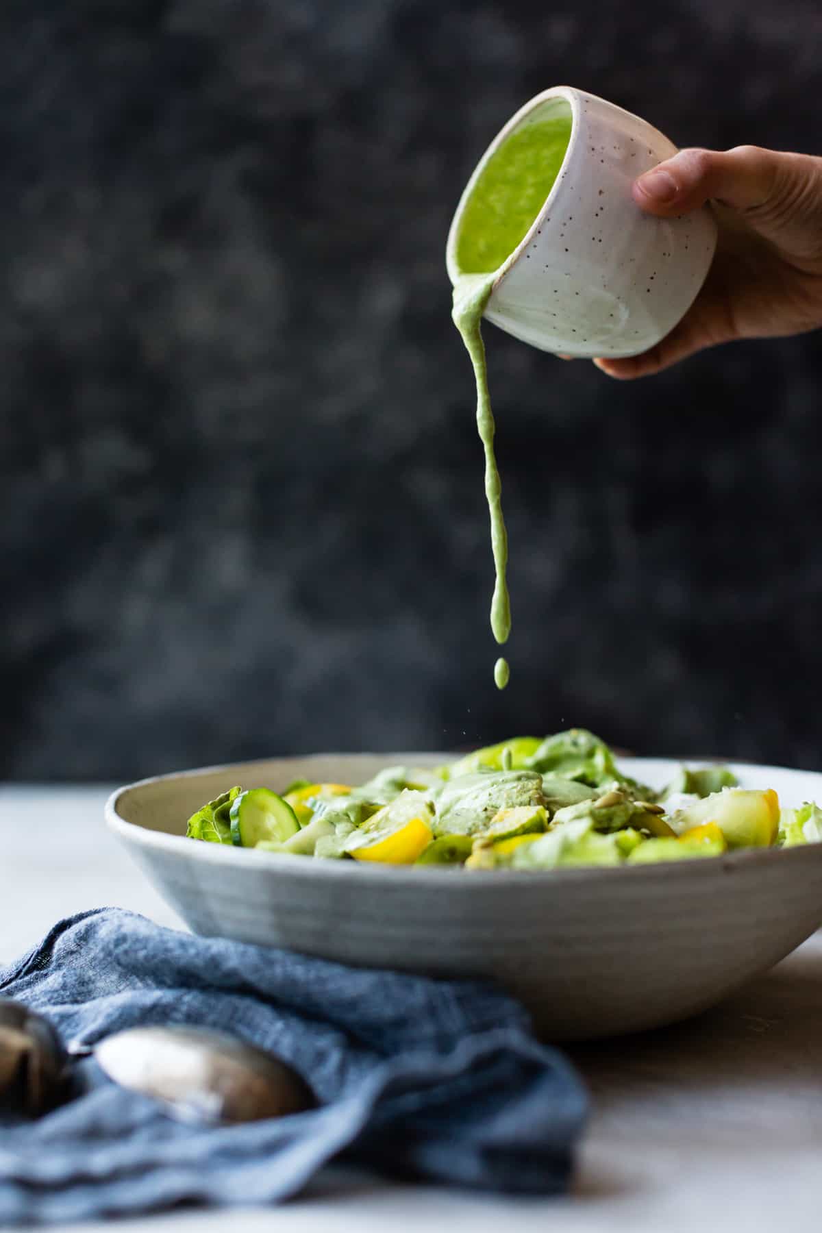 pouring creamy cashew green goddess dressing on salad 