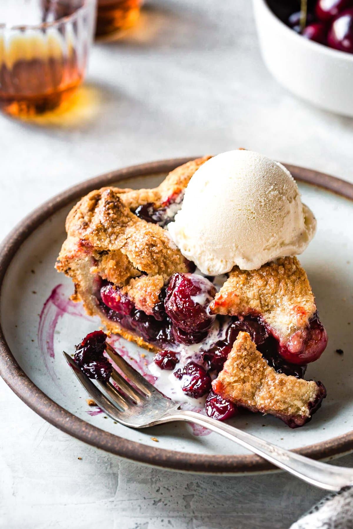 A slice of cherry pie sits on a plate topped with melty ice cream