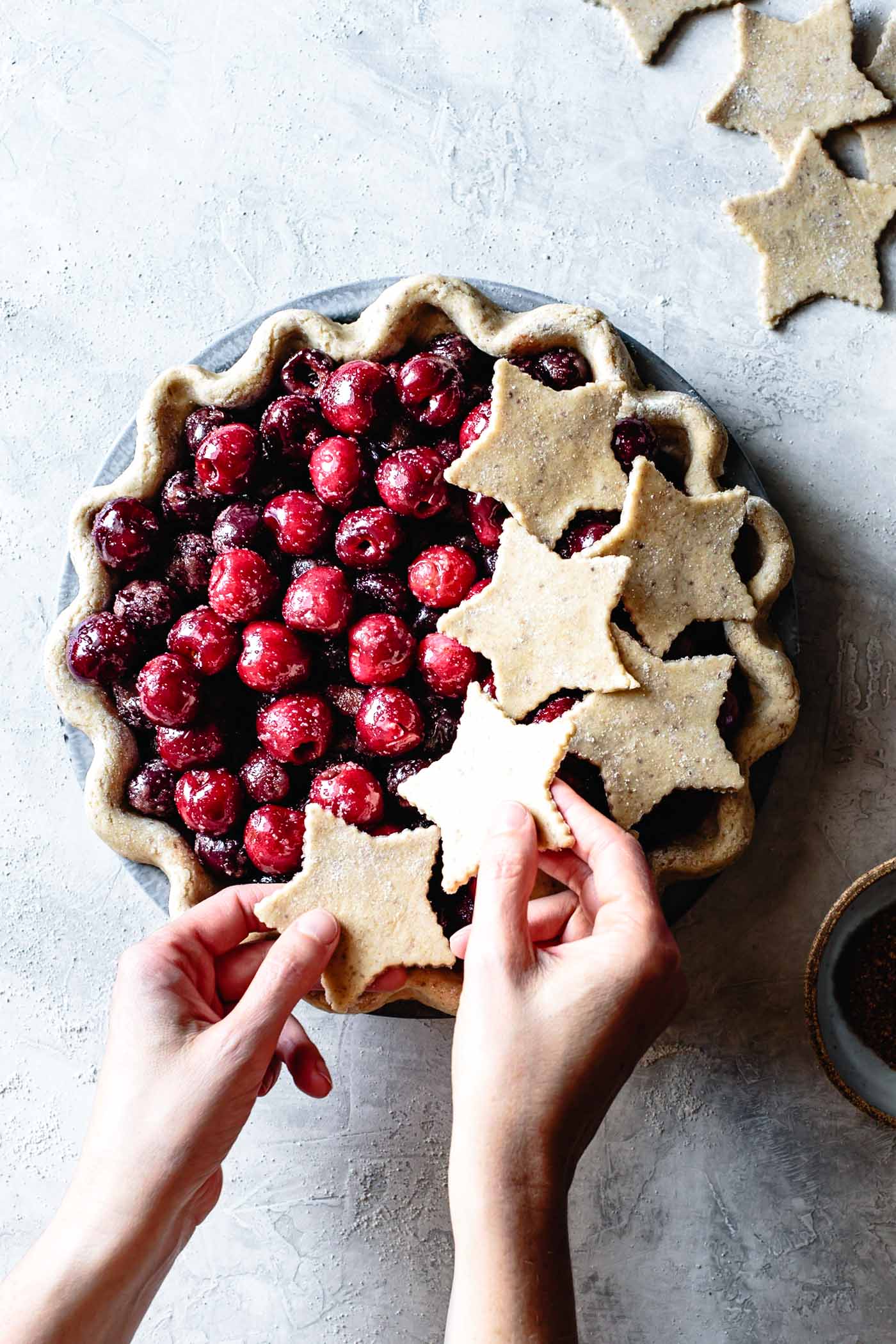 hands are placing star-shaped dough cut-outs over the cherries