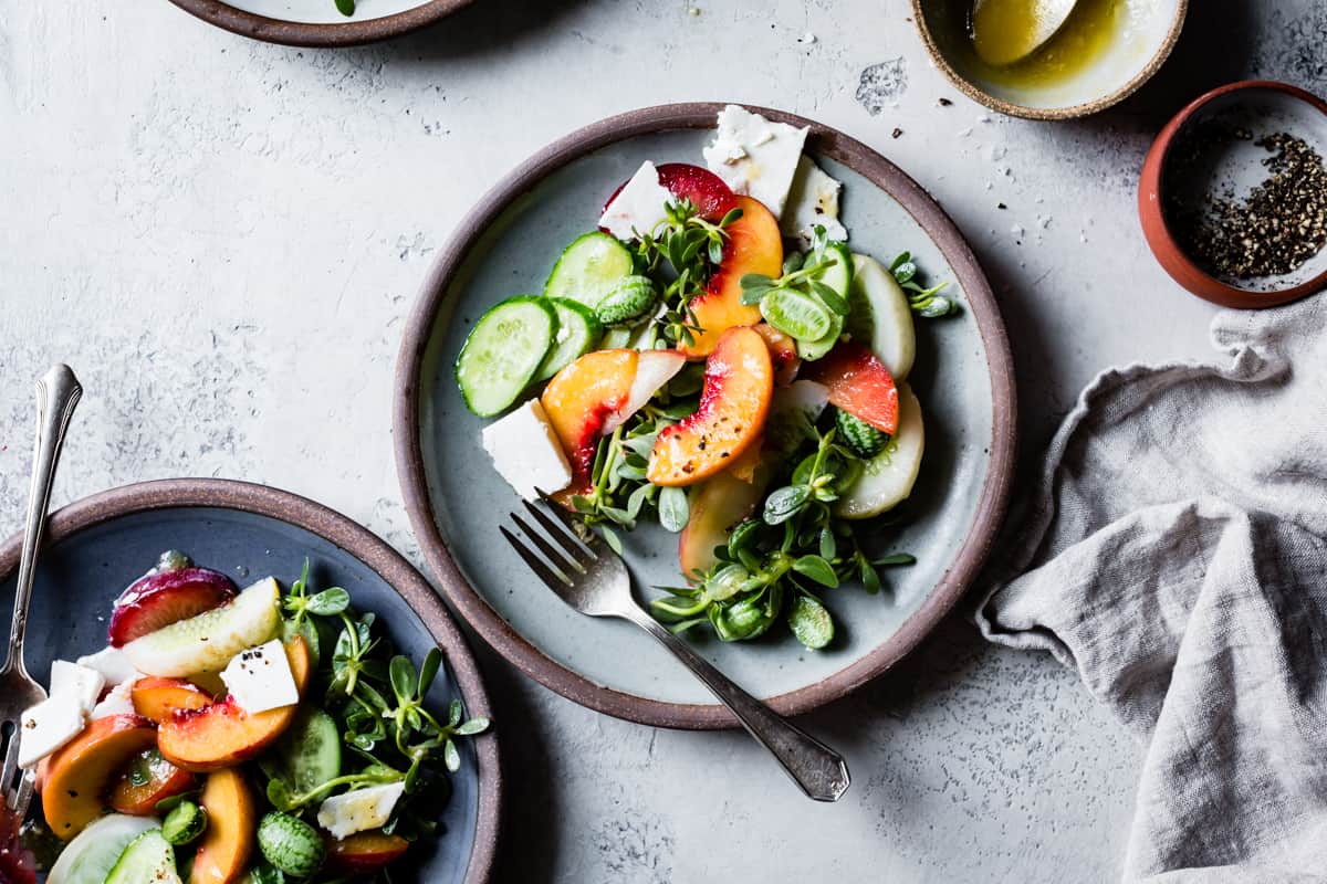 two plates of Stone Fruit Cucumber Salad with Ricotta Salata, Purslane, and Golden Balsamic Miso Vinaigrette