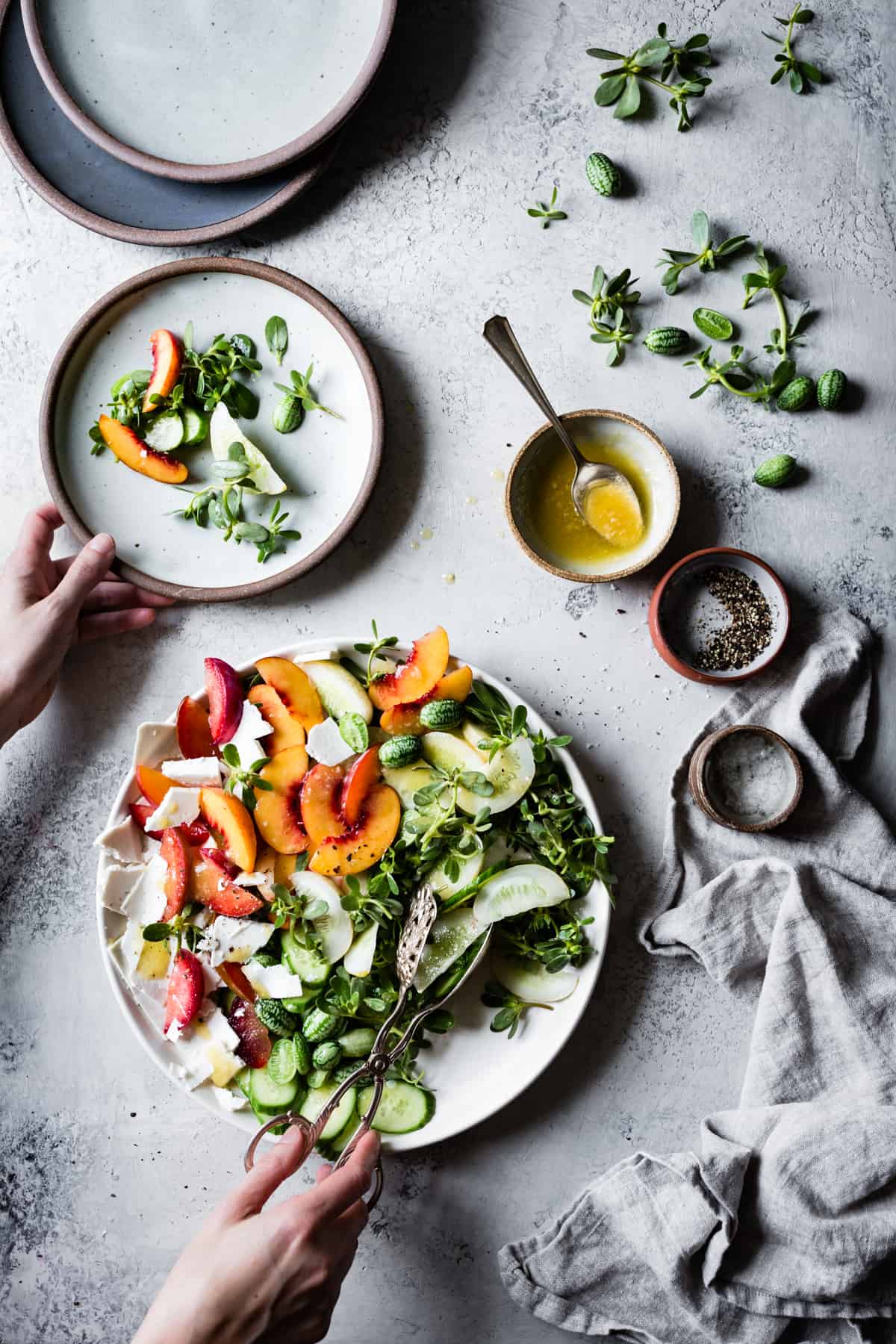 hands holding plates of Stone Fruit Cucumber Salad with Ricotta Salata, Purslane, and Golden Balsamic Miso Vinaigrette