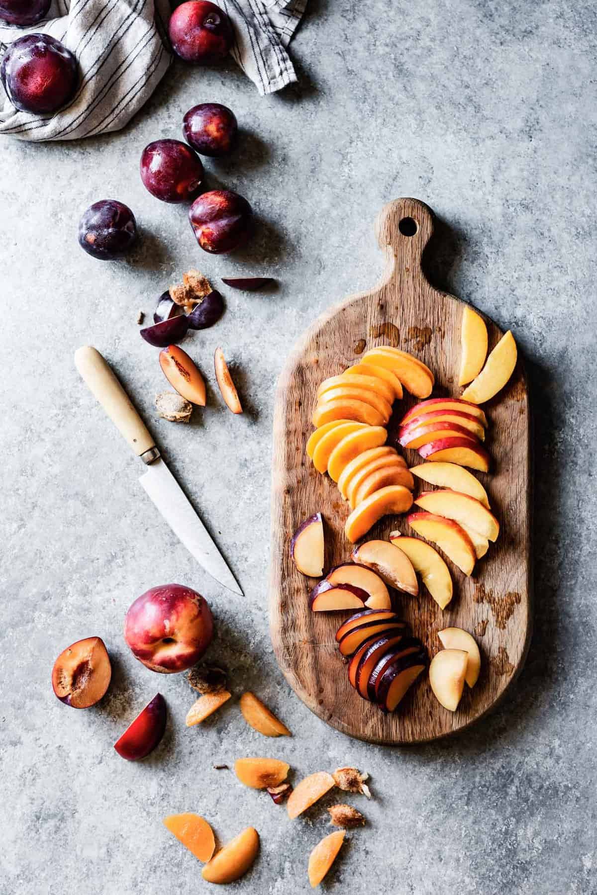 slices of apricots, plums, and nectarines on a rusting wooden paddle cutting board