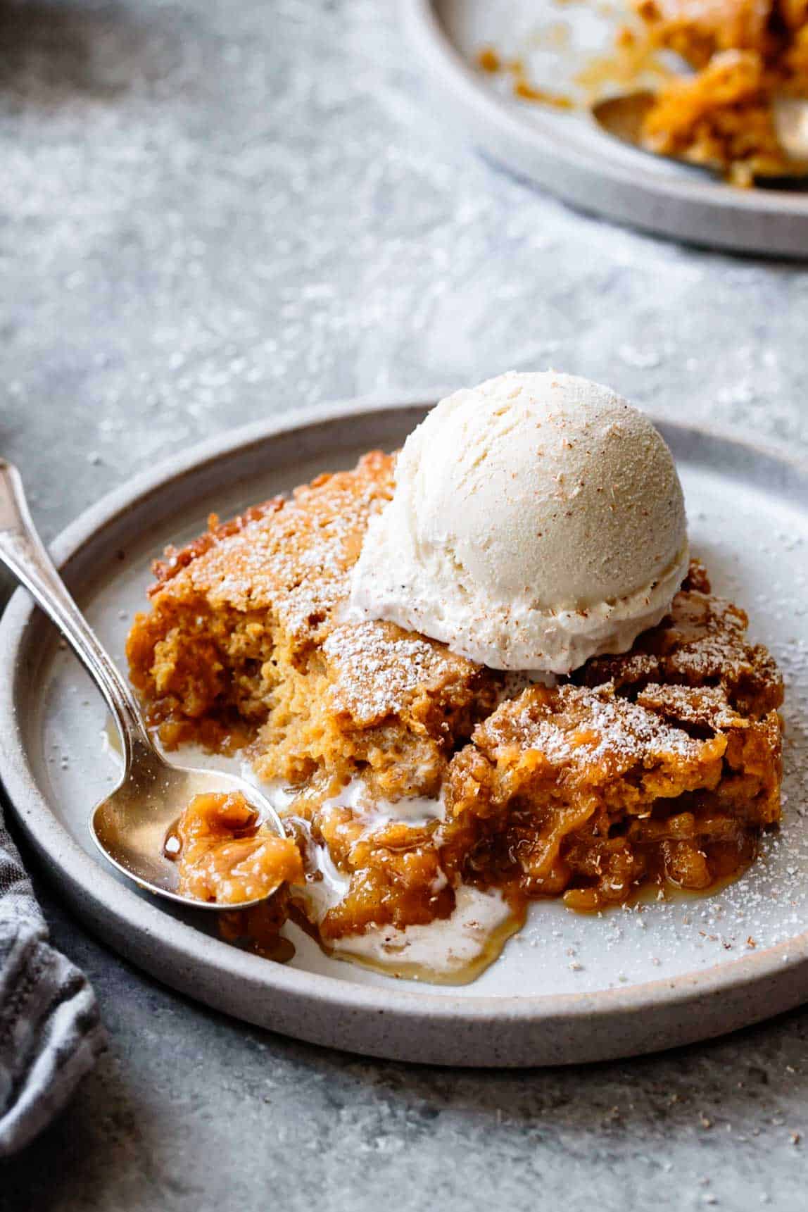 a gooey piece of Gluten Free Pumpkin Pudding Cake with a scoop of ice cream on a slate plate looking seductive