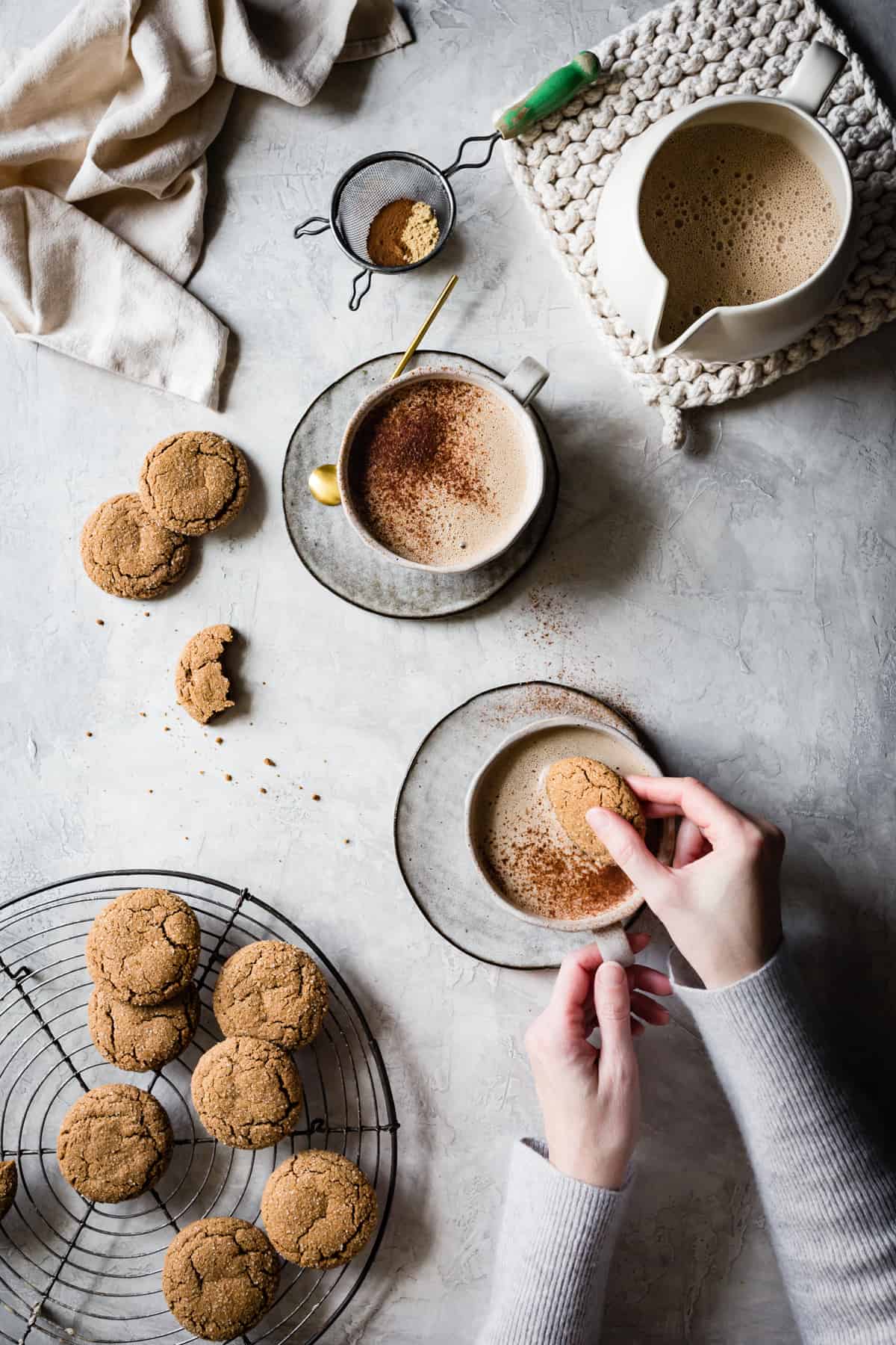 A hand is dipping gluten-free ginger molasses cookies into a mug of creamy gingersnap latte goodness