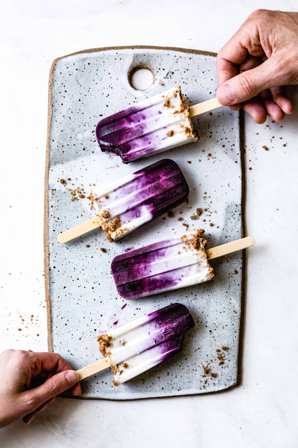 hands holding Blueberry Chèvre Cheesecake Popsicles