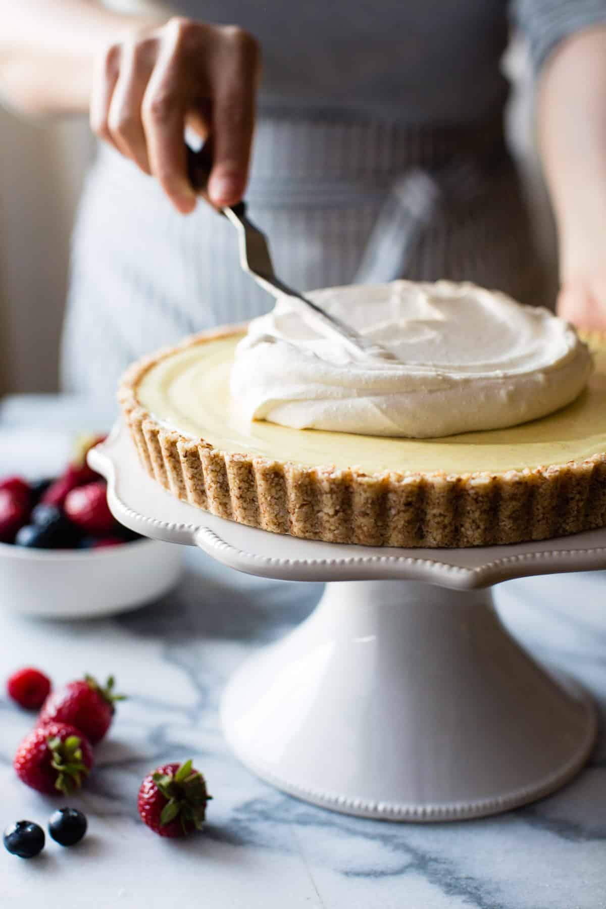 woman spreading whipped cream over lemon tart on white cake stand