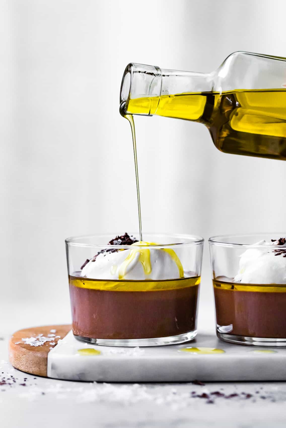drizzling olive oil onto pots de creme in glasses on marble board