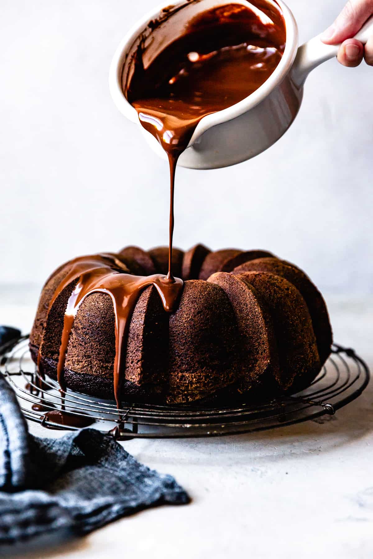 Glossy chocolate ganache is being poured over a handsome brown bundt cake