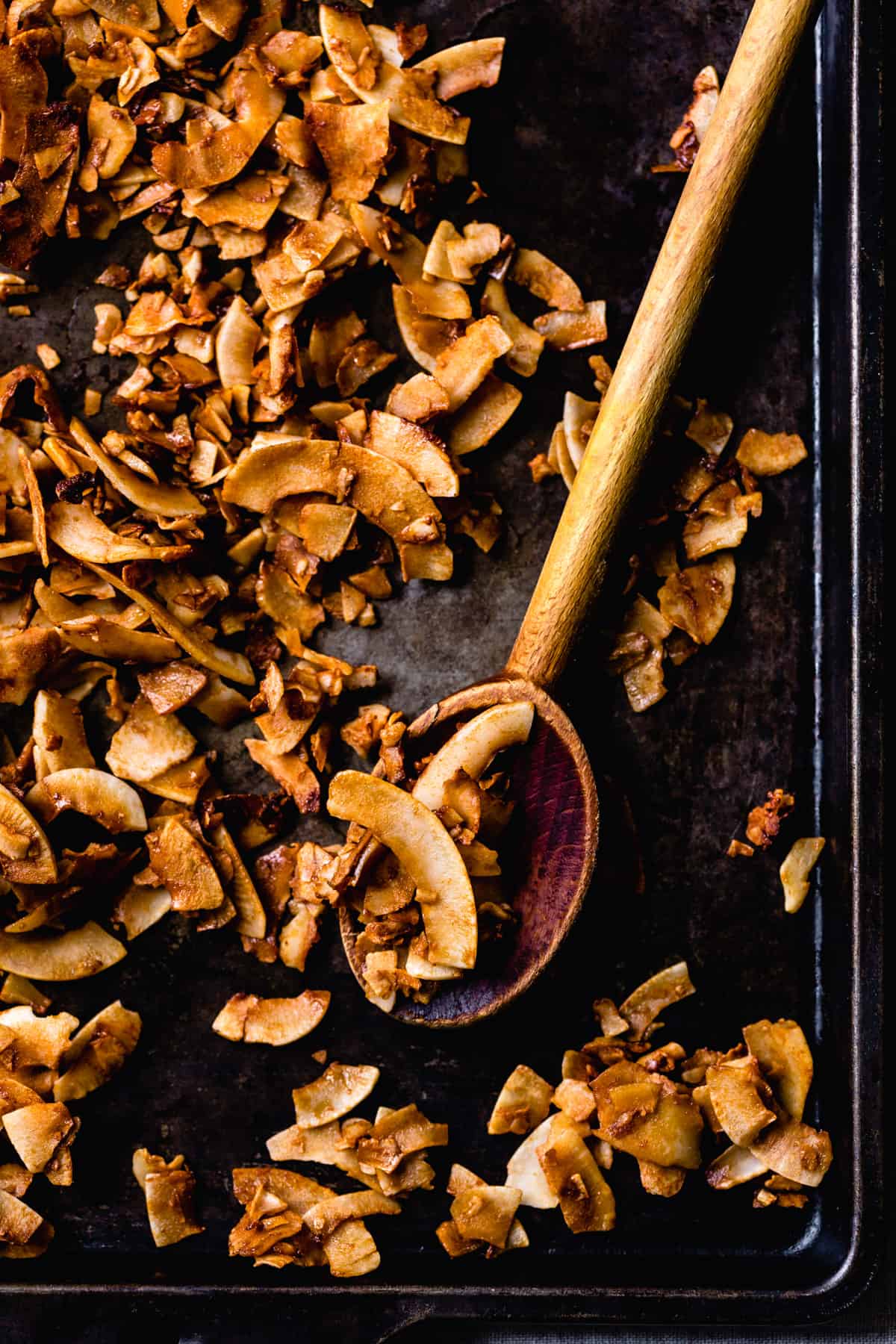 golden flakes of crispy coconut have been baked on a dark sheet pan
