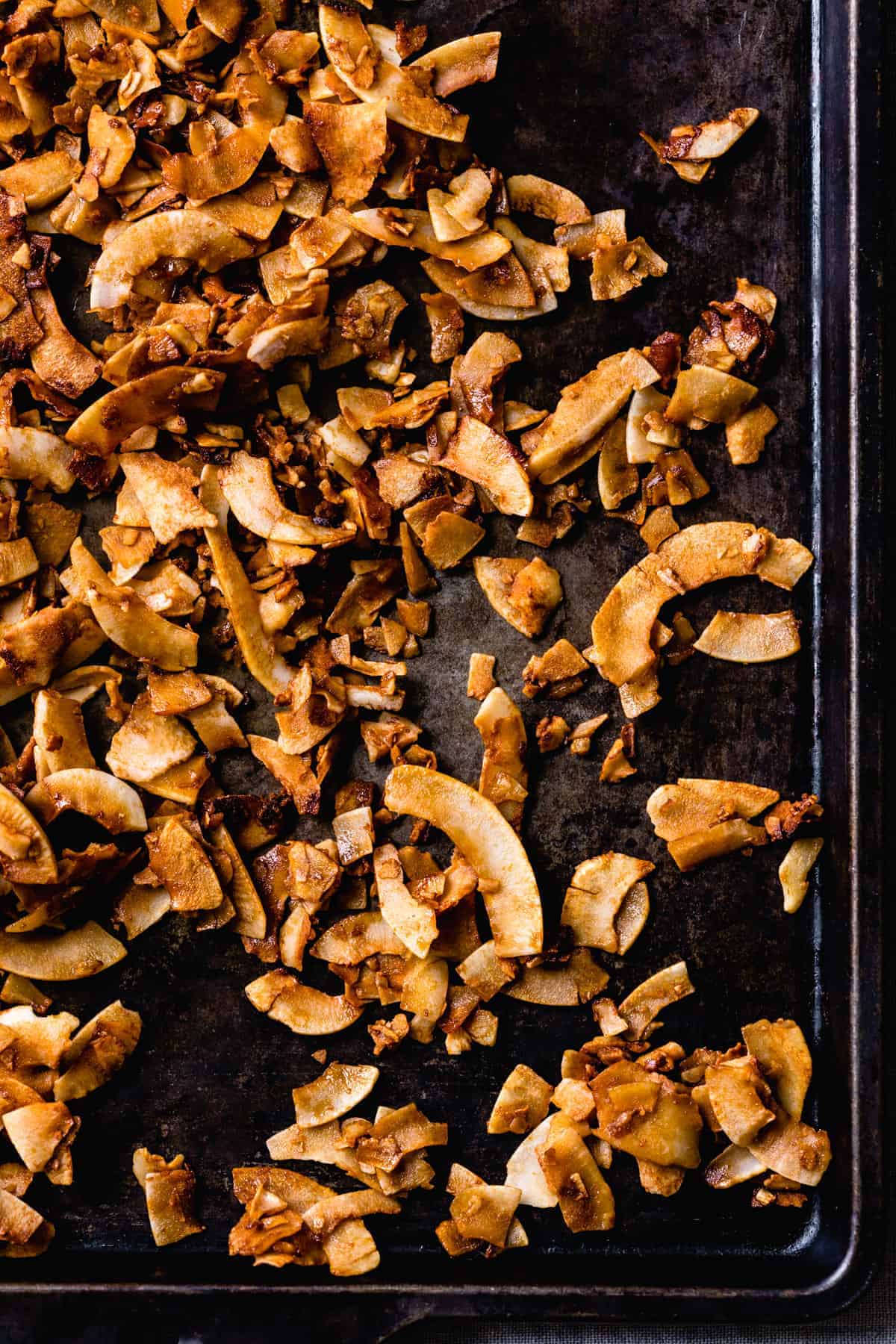 Freshly baked coconut bacon on a dark sheet pan