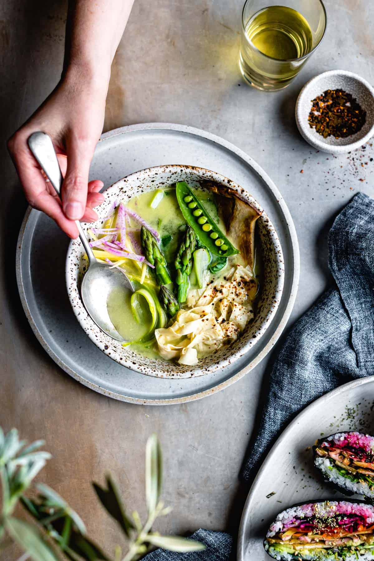 hand with spoon in bowl of Spring Vegan Miso Soup with Yuba Gluten-Free Noodles