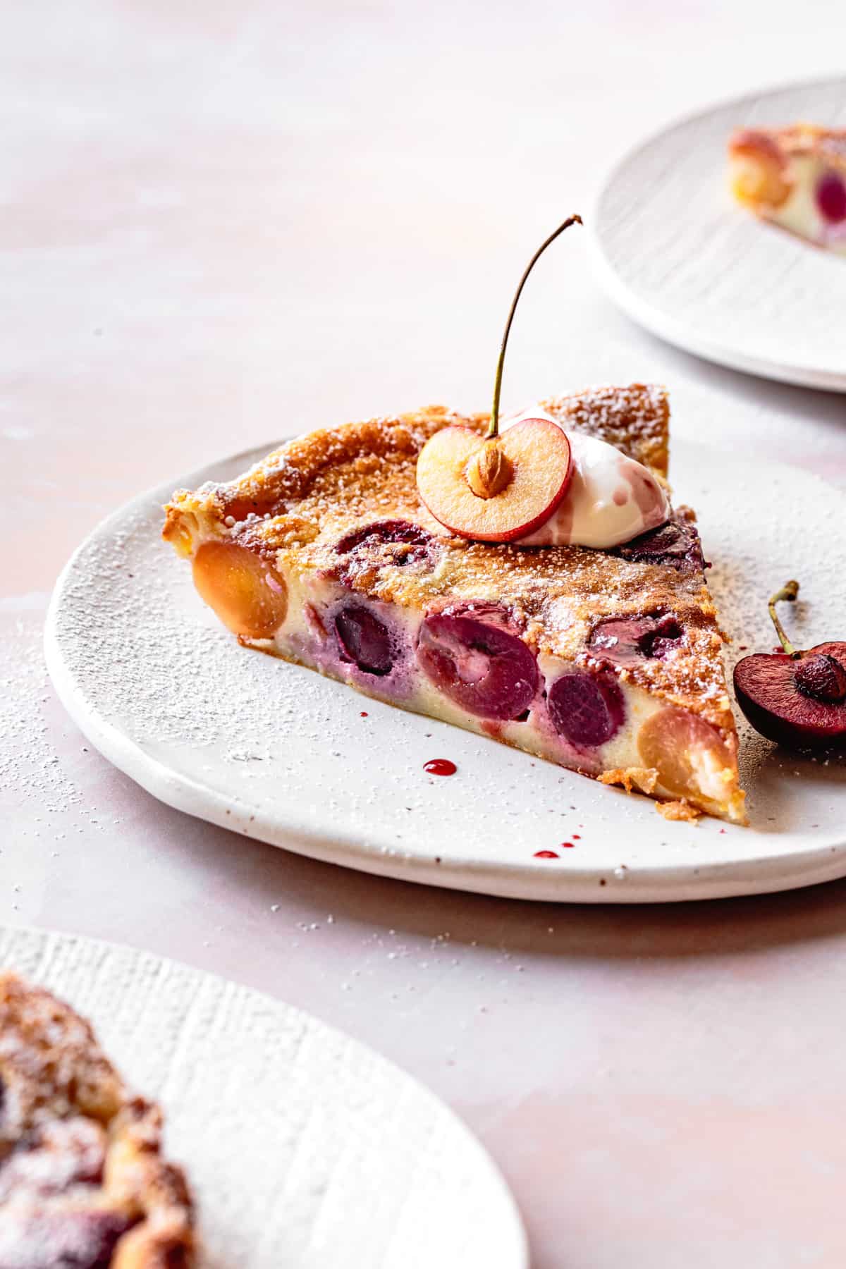 Gluten-Free Cherry Clafoutis slice on a plate with creme fraiche and sliced cherry on top