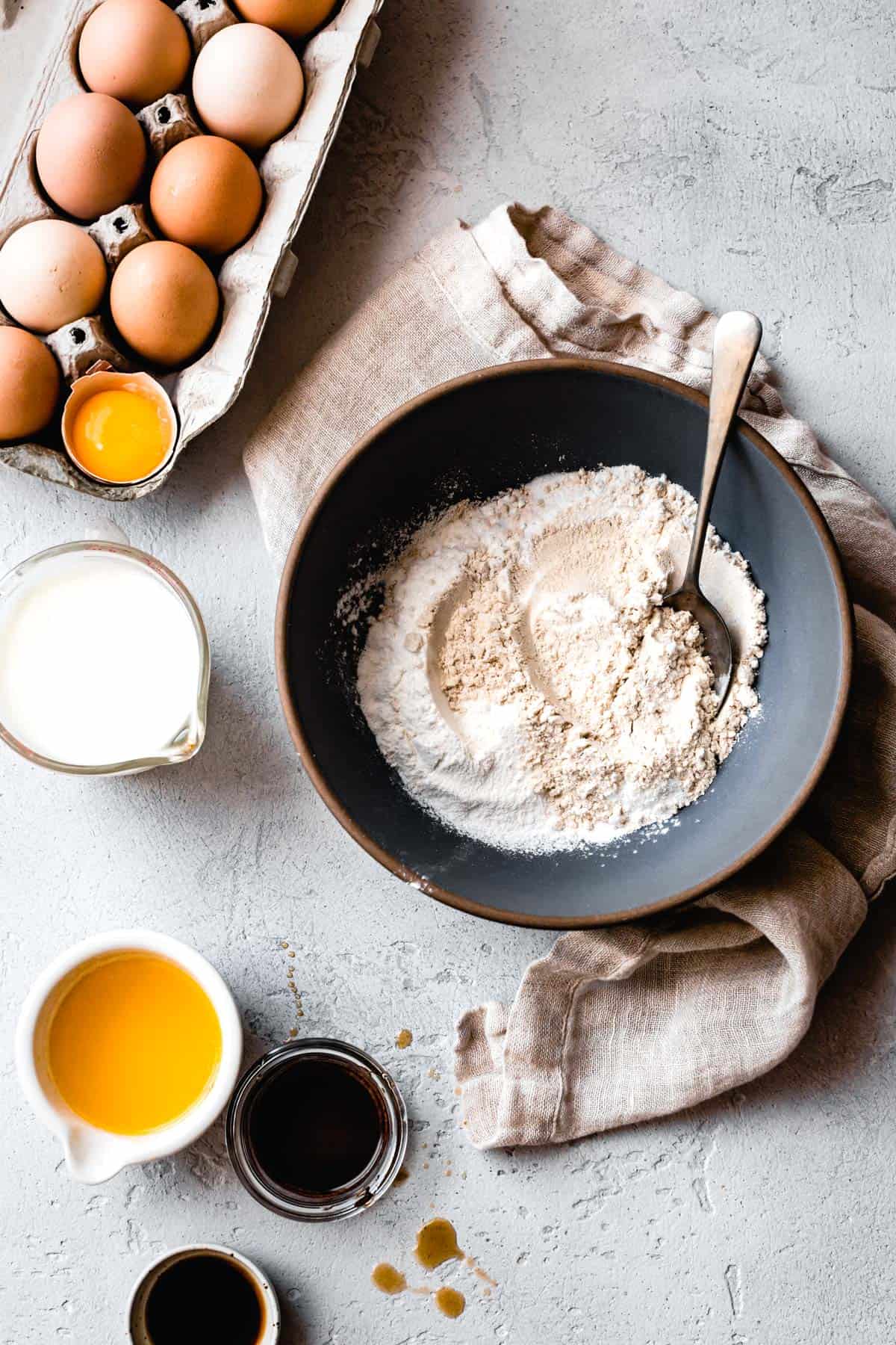 Ingredients and flours for gluten free pancakes are arranged on a gray plaster surface