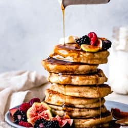pouring maple syrup over a stack of gluten-free buttermilk pancakes