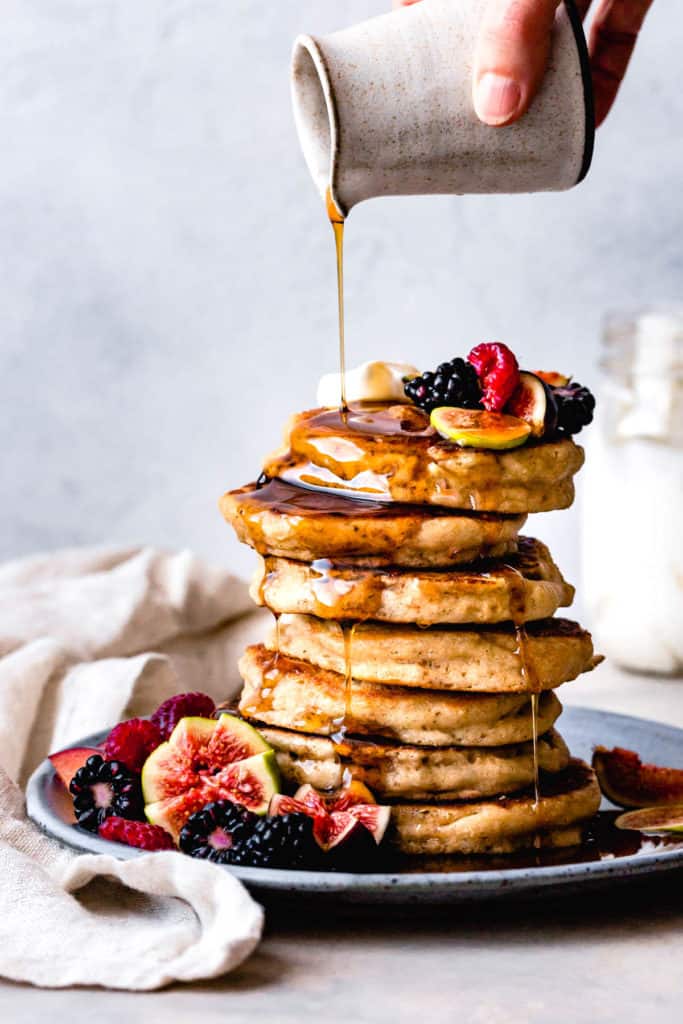 pouring maple syrup over a stack of gluten-free buttermilk pancakes