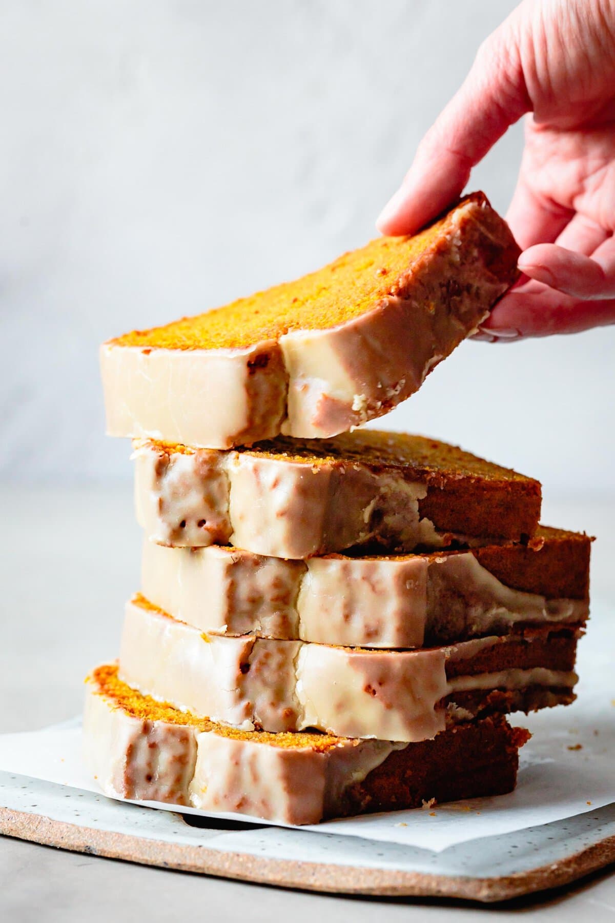 a hand is lifting a piece of pumpkin bread finished with maple glaze