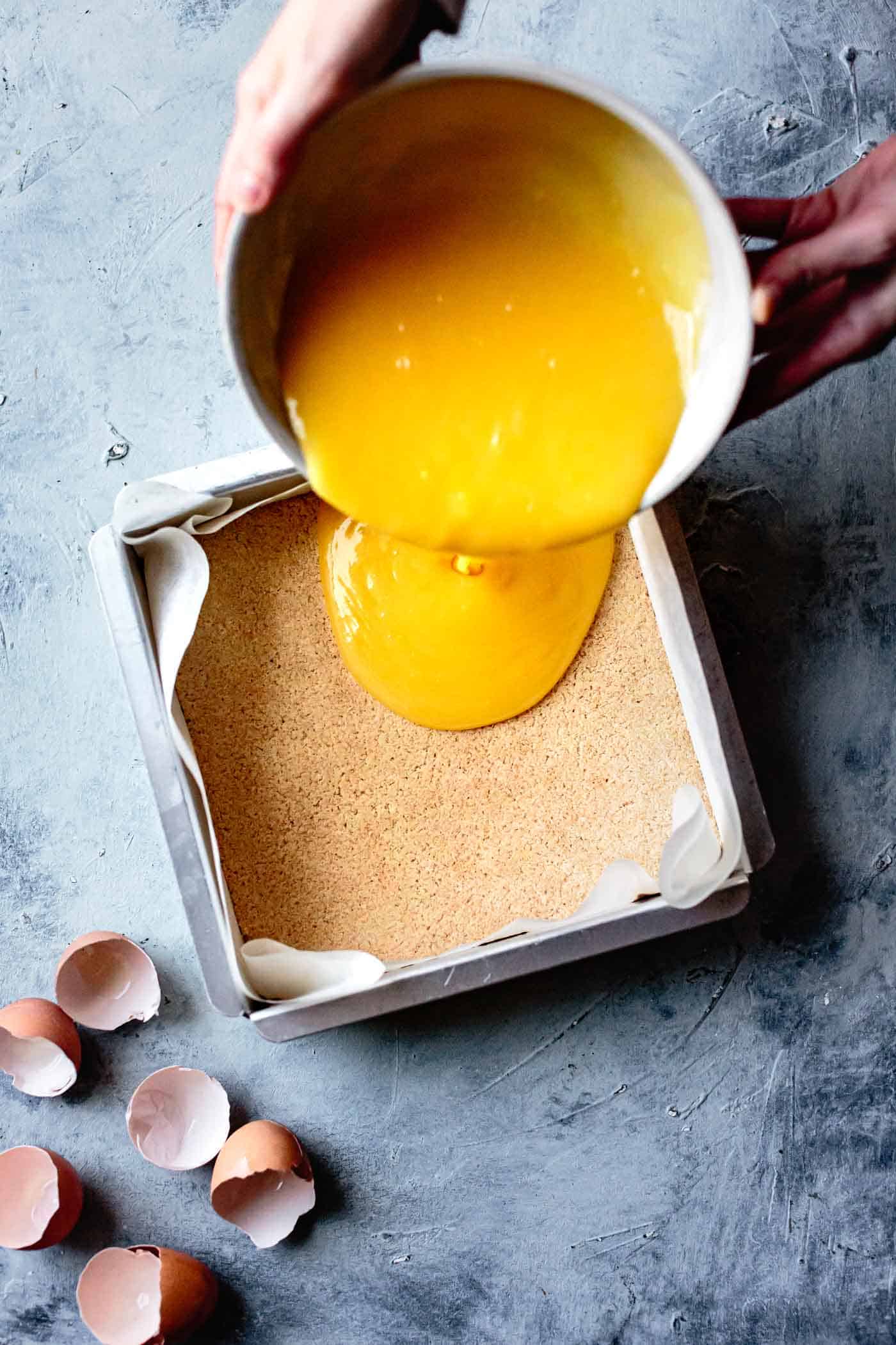 Pouring lemon curd into almond flour crust for gluten-free easy lemon squares