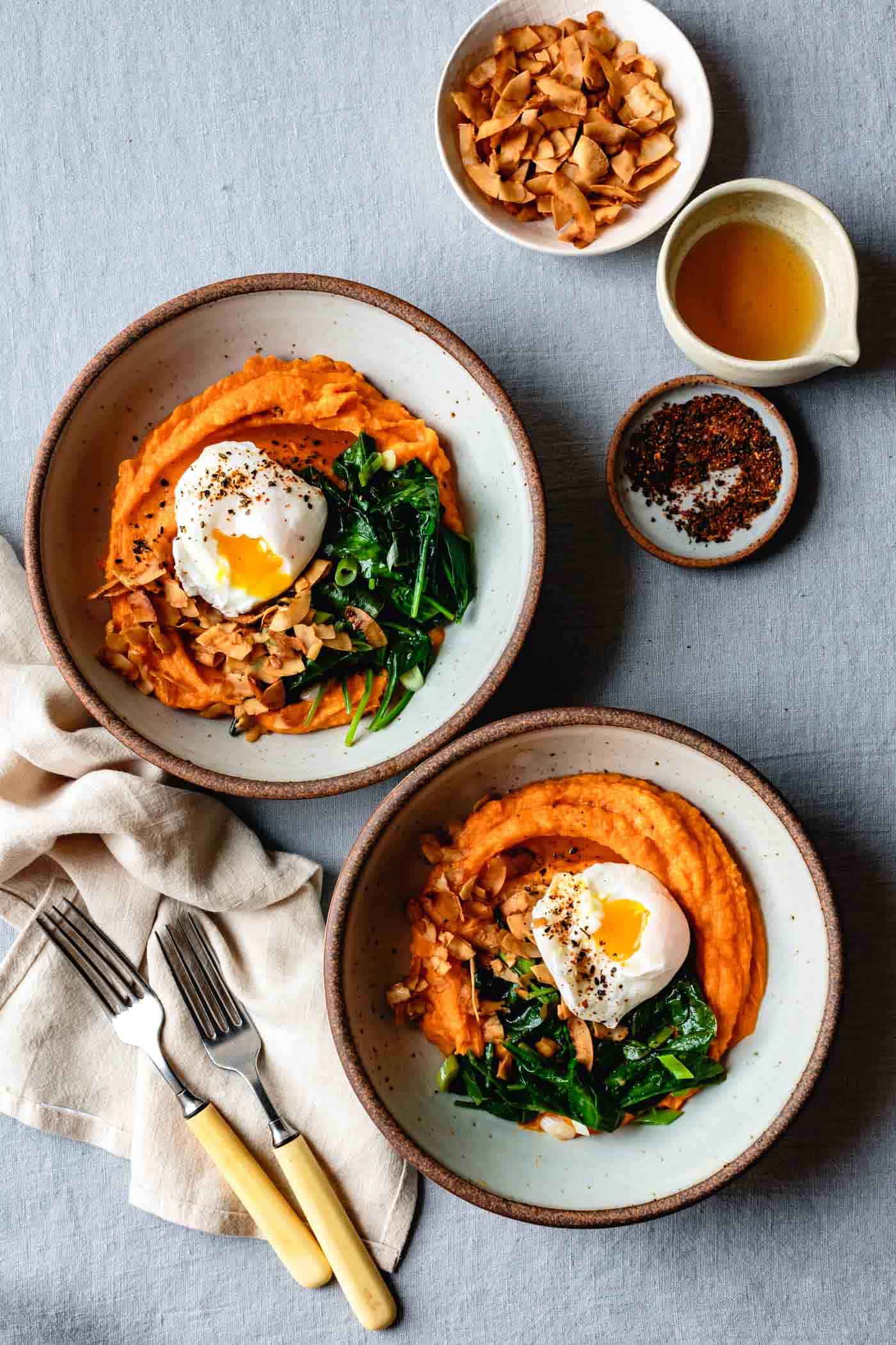 two sweet potato breakfast bowls are arranged on a linen tabletop with forks and napkins, ready to eat!