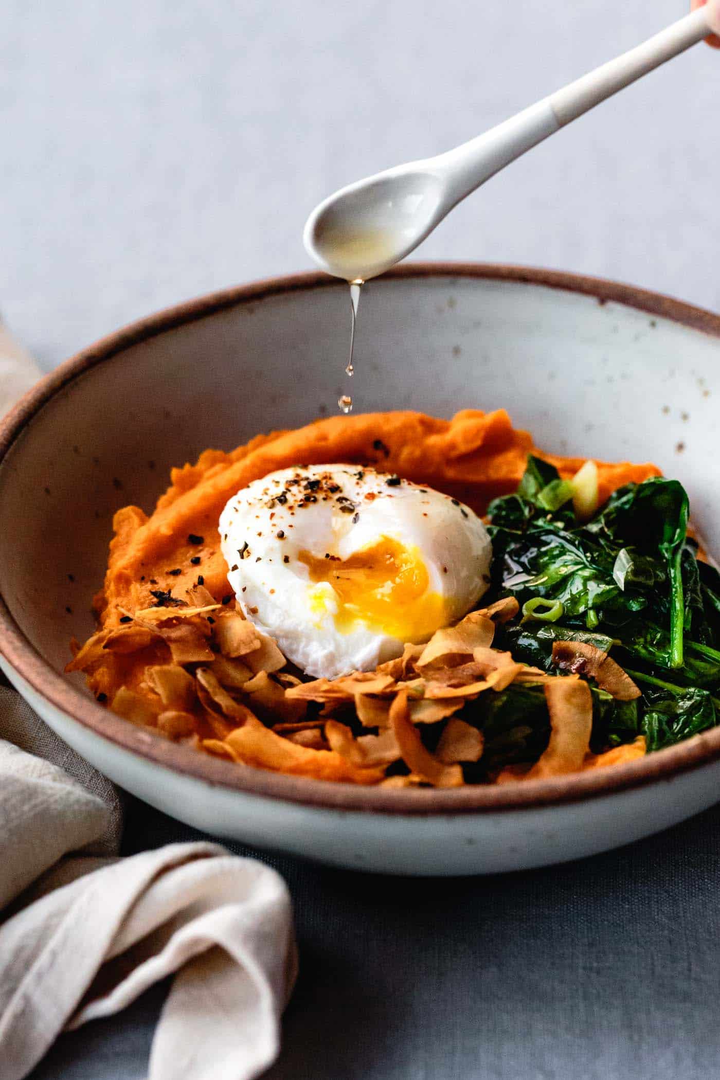 drizzling sesame oil over sweet potato breakfast bowl with egg