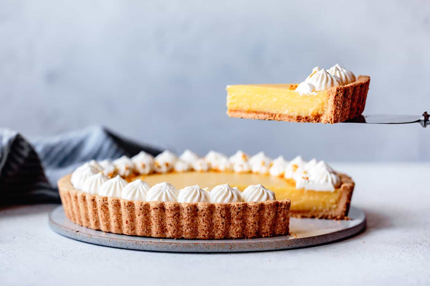 a slice of lemon curd tart is being lifted from a whole tart